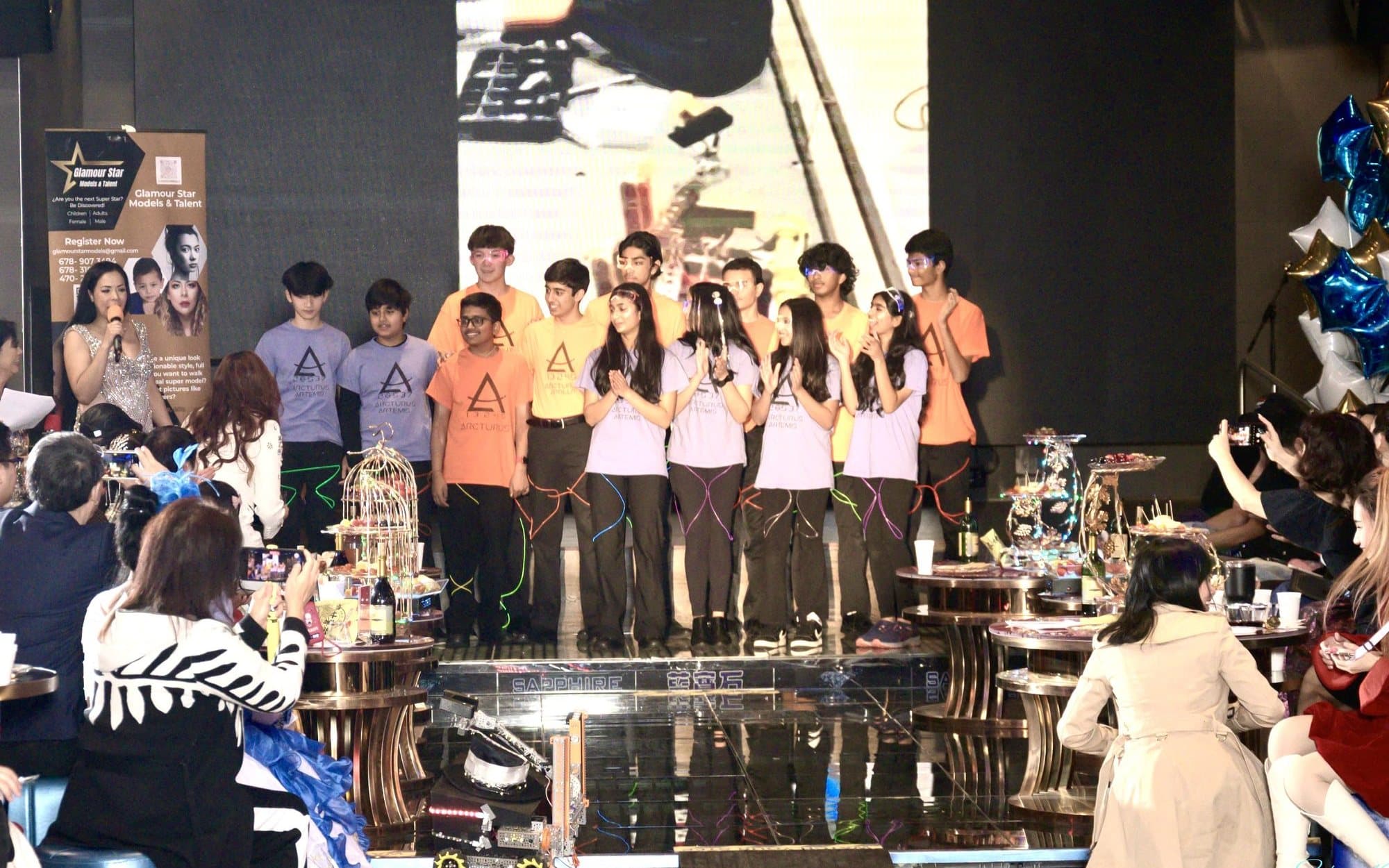 Arcturus team members lined up on stage at the Fashion Meets Tech show, with robots on the runway